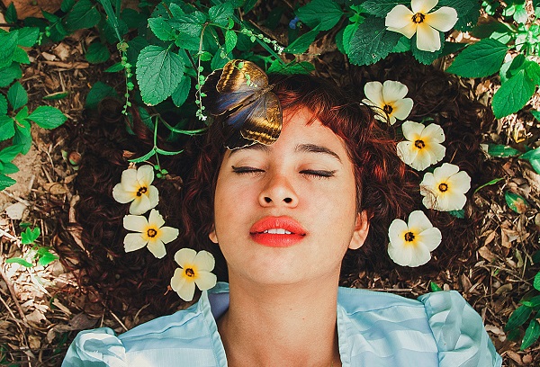 A woman laying in a garden with her eyes closed, practicing mindfullness.